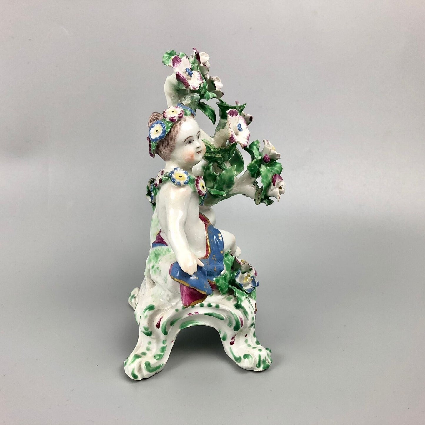 A pair of Bow putti with rococo C-scroll bases and bocage c.1760
