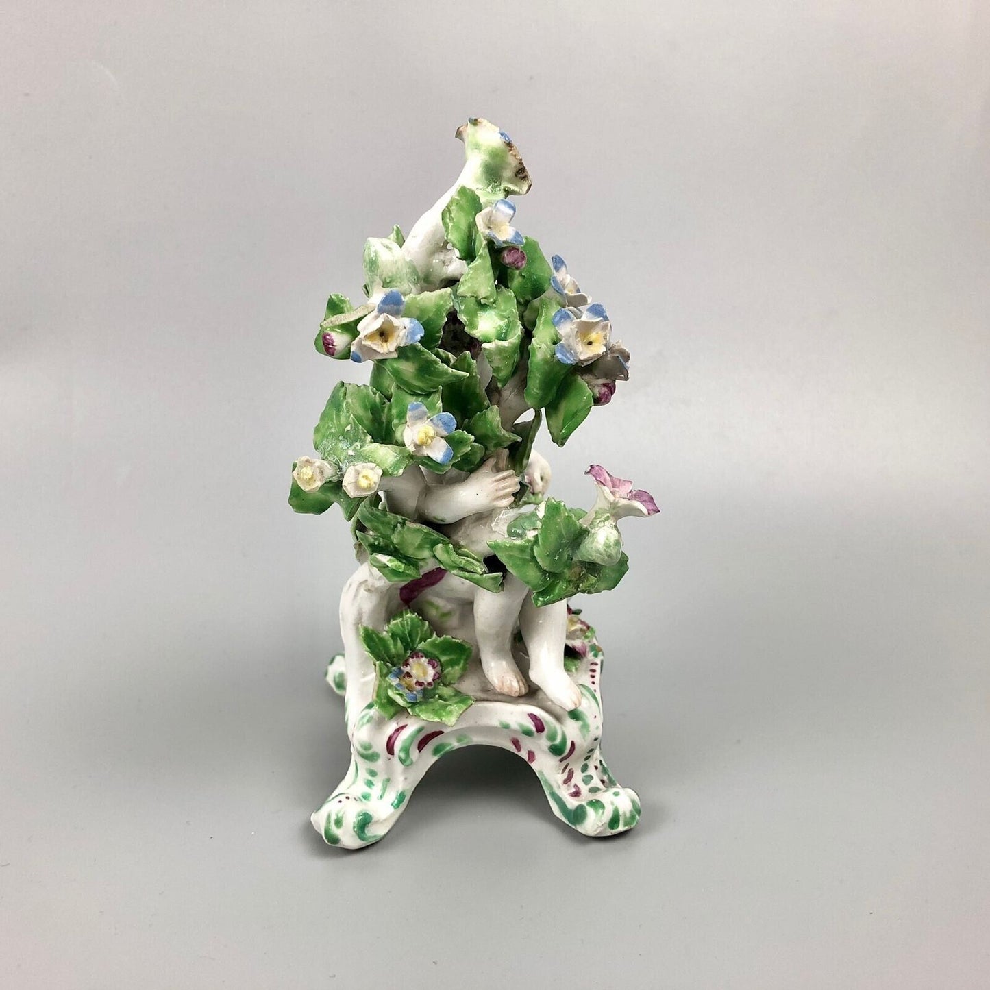 A pair of Bow putti with rococo C-scroll bases and bocage c.1760