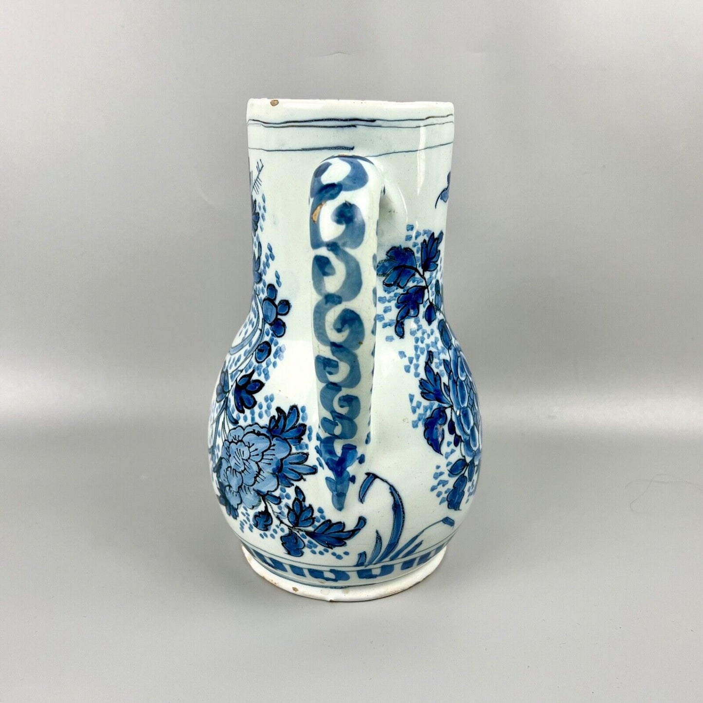An early 18thc Dutch Delft jug painted with peacocks, holey rocks and peonies