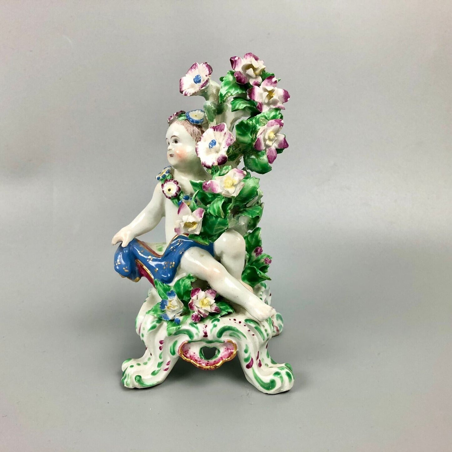 A pair of Bow putti with rococo C-scroll bases and bocage c.1760