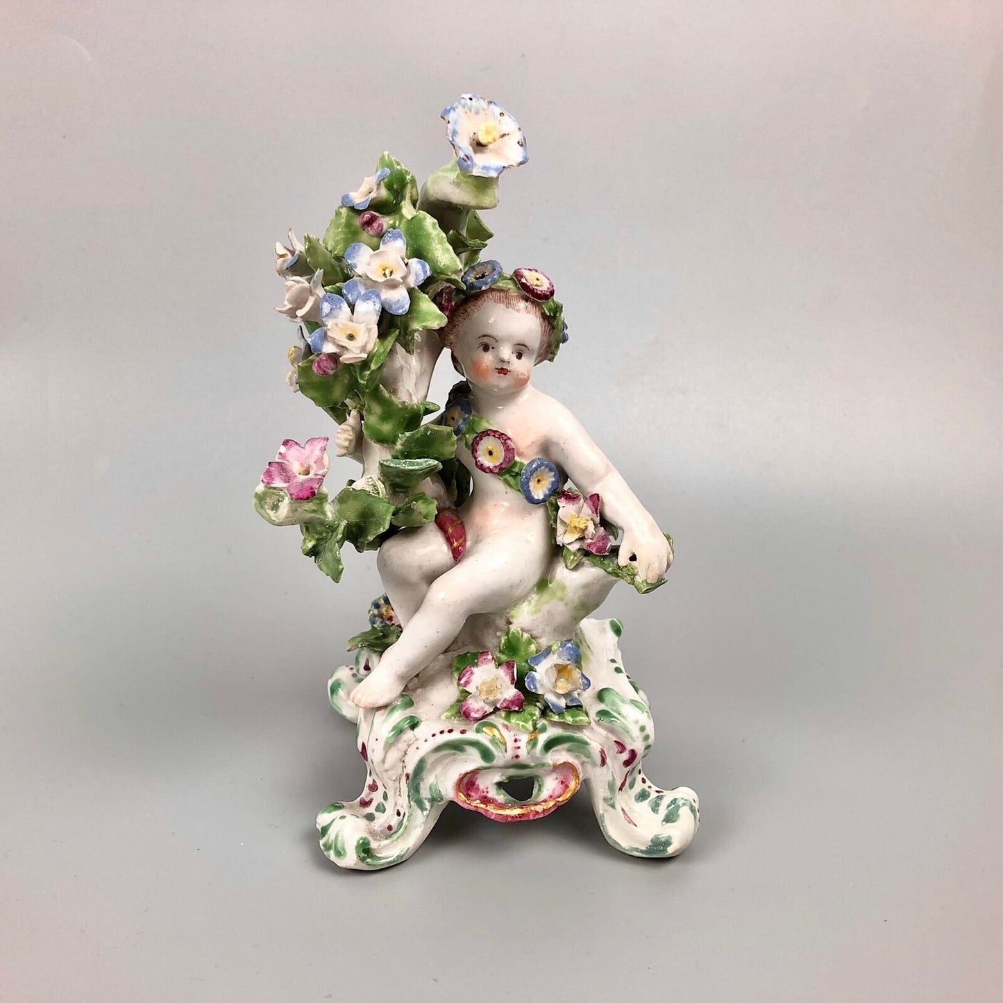 A pair of Bow putti with rococo C-scroll bases and bocage c.1760
