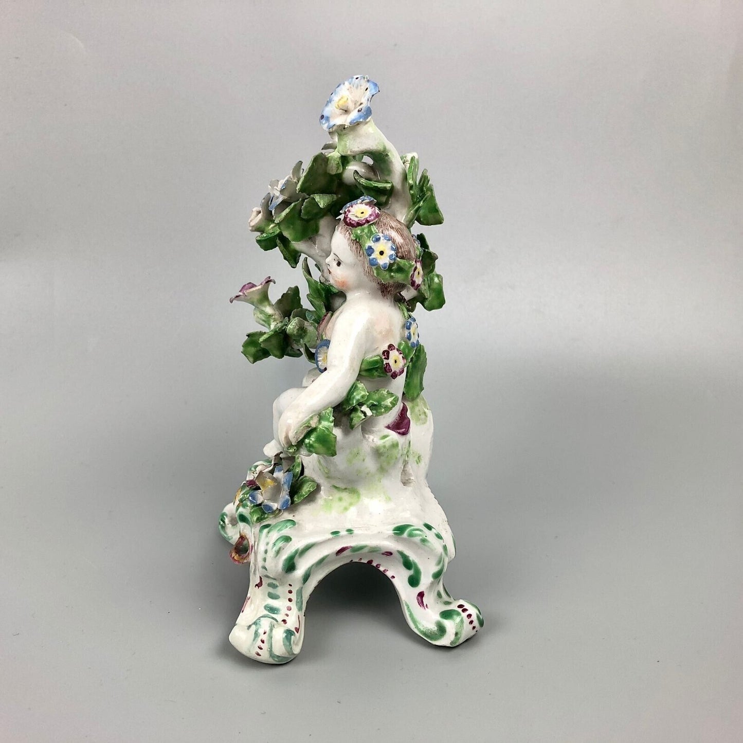 A pair of Bow putti with rococo C-scroll bases and bocage c.1760