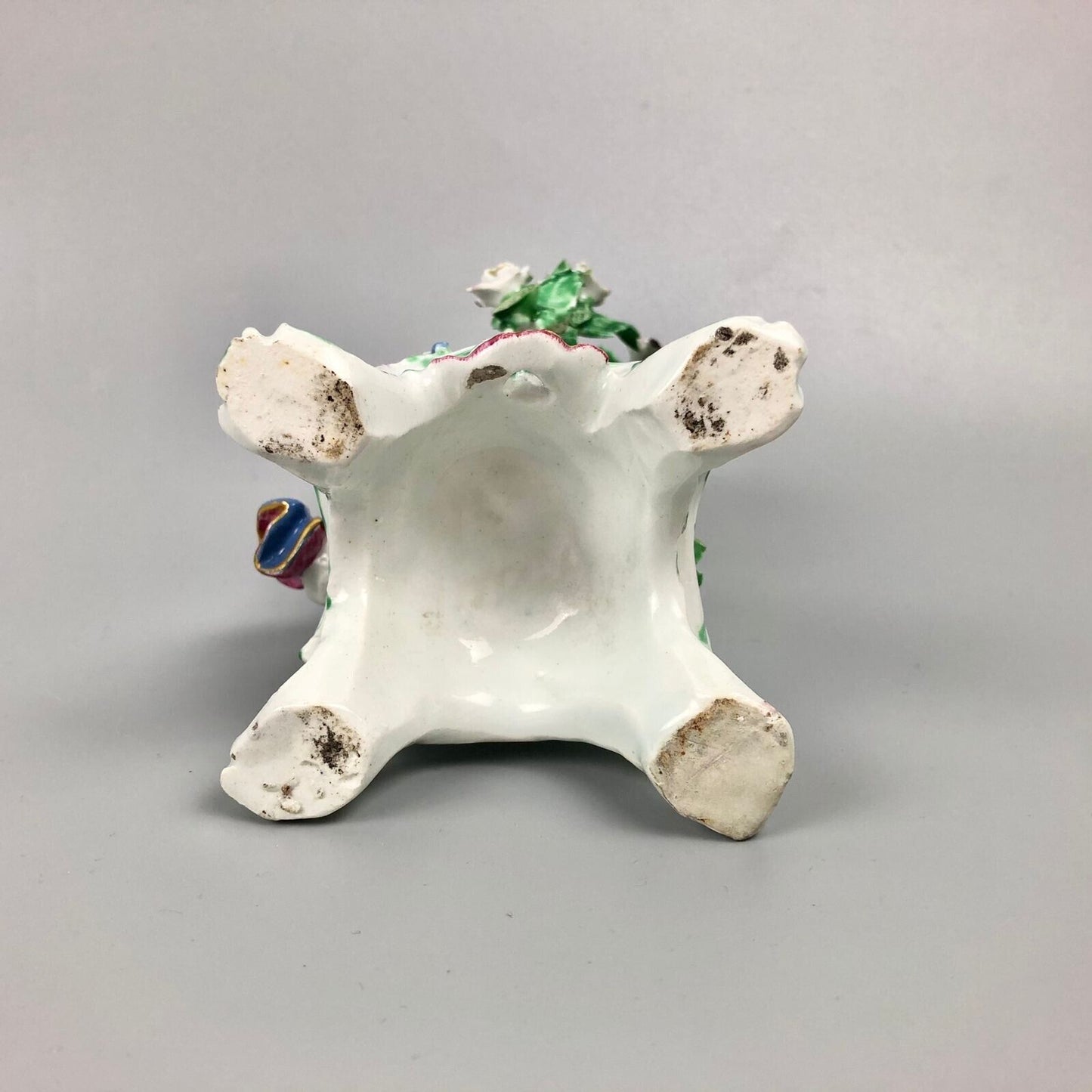 A pair of Bow putti with rococo C-scroll bases and bocage c.1760