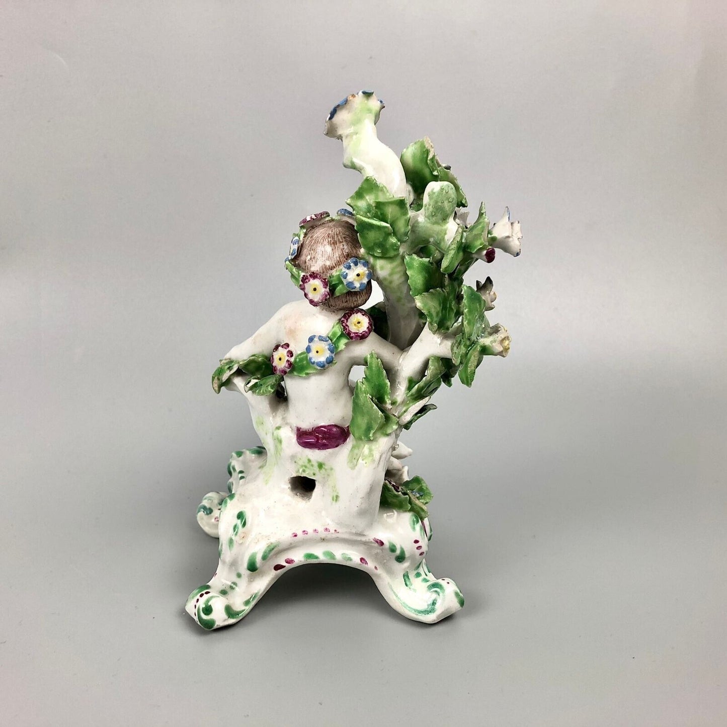 A pair of Bow putti with rococo C-scroll bases and bocage c.1760