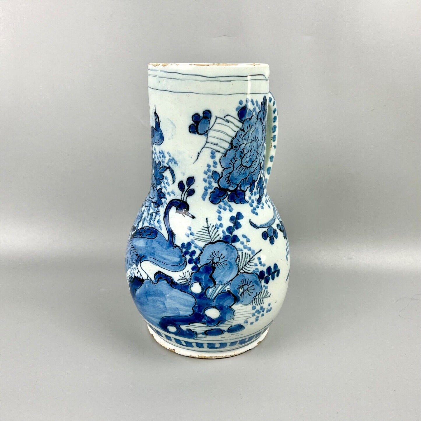An early 18thc Dutch Delft jug painted with peacocks, holey rocks and peonies