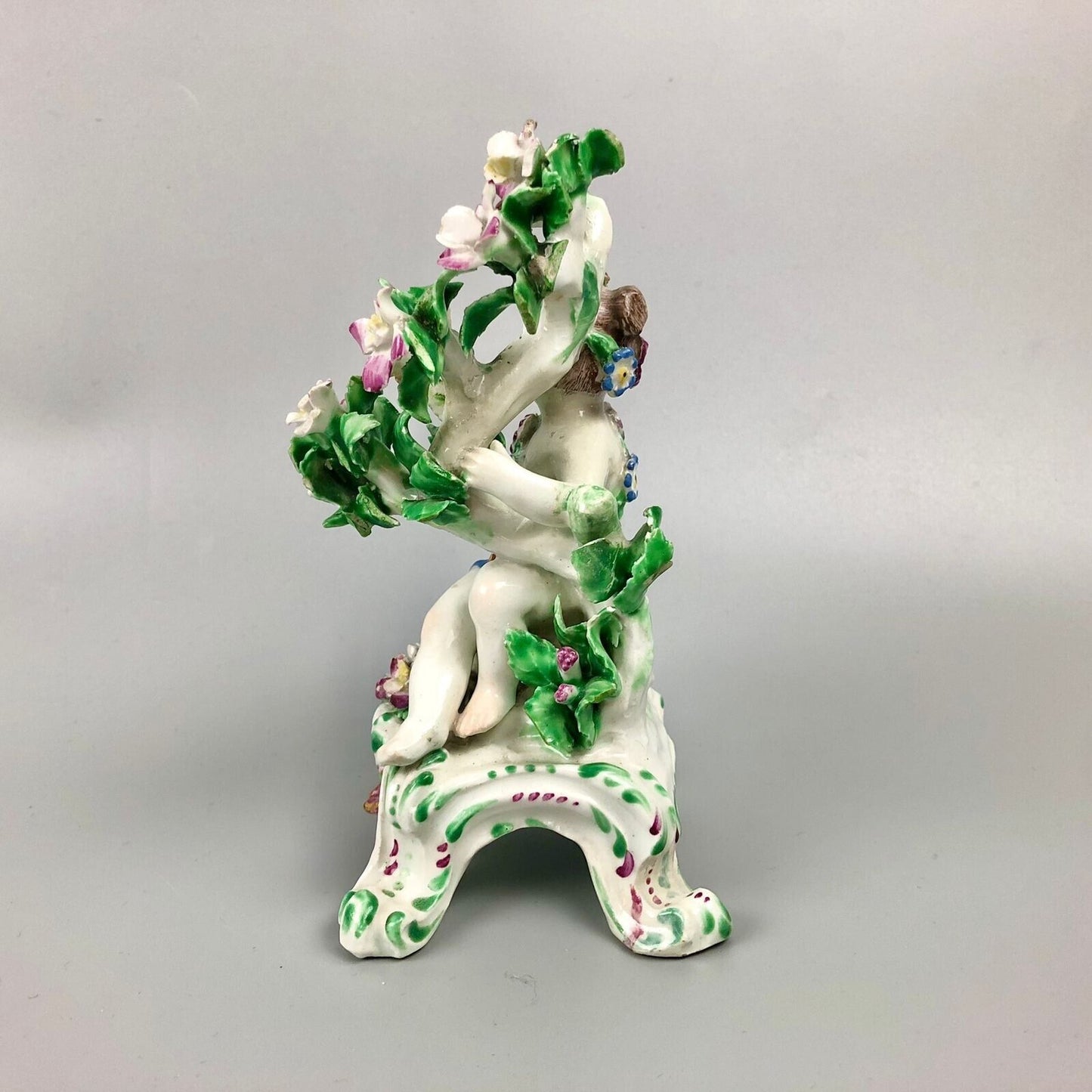 A pair of Bow putti with rococo C-scroll bases and bocage c.1760