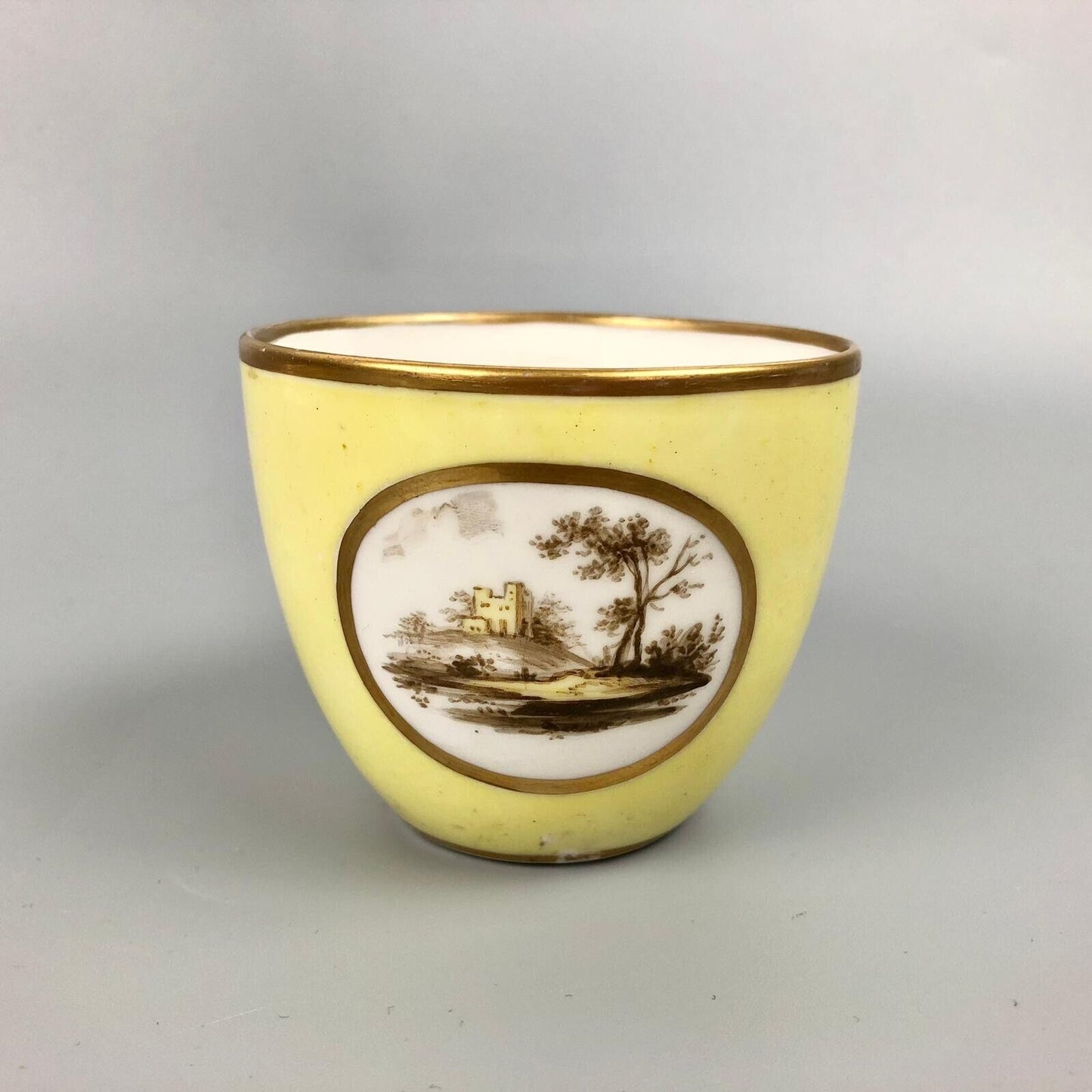 A Pinxton coffee cup and saucer in yellow ground and sepia landscapes. C.1796-9