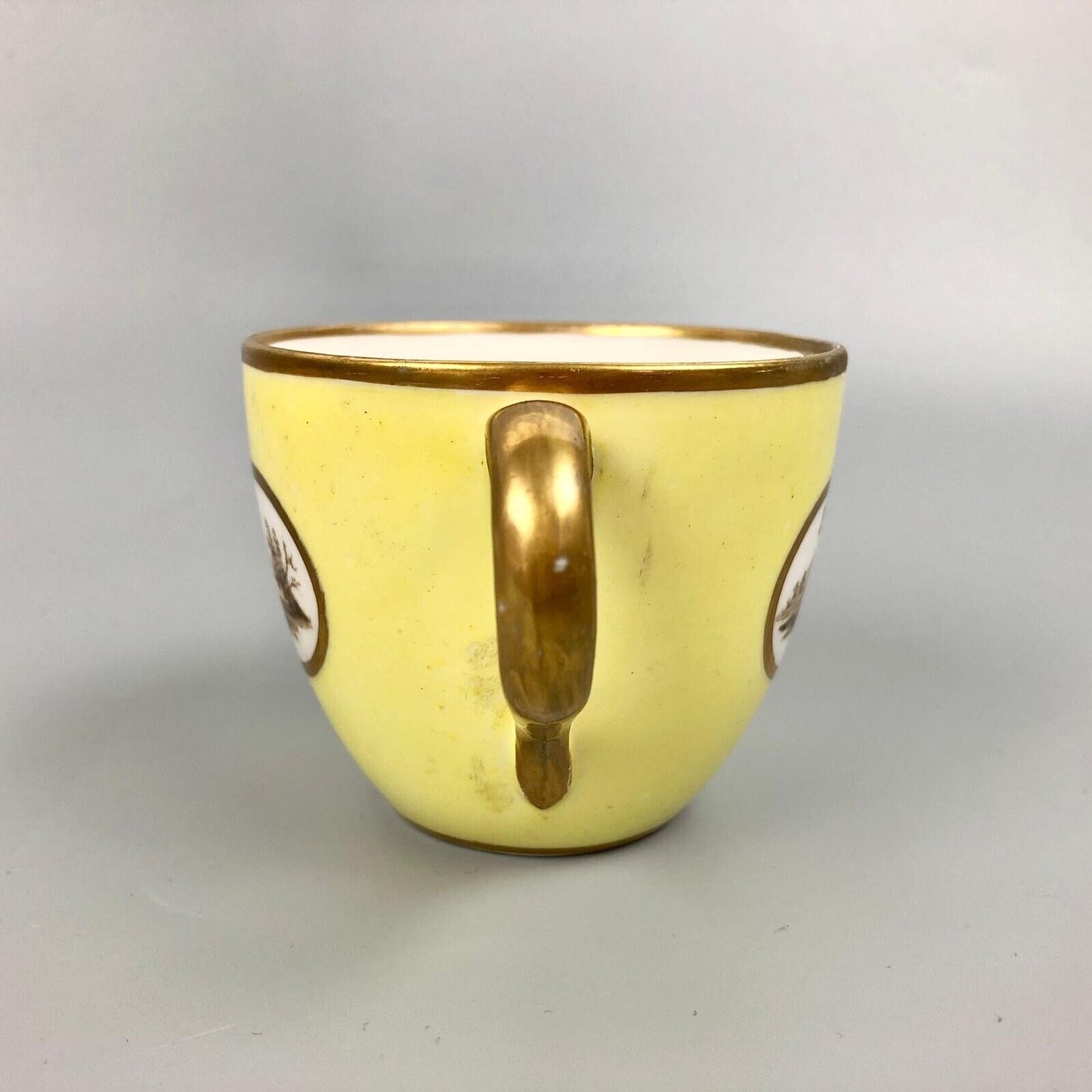 A Pinxton coffee cup and saucer in yellow ground and sepia landscapes. C.1796-9