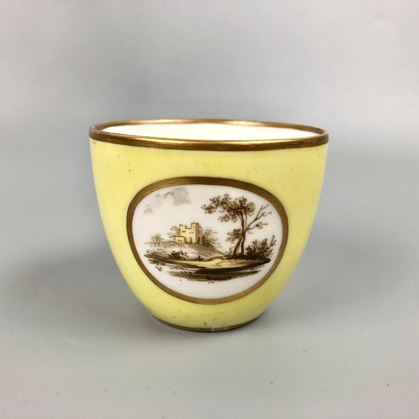 A Pinxton coffee cup and saucer in yellow ground and sepia landscapes. C.1796-9