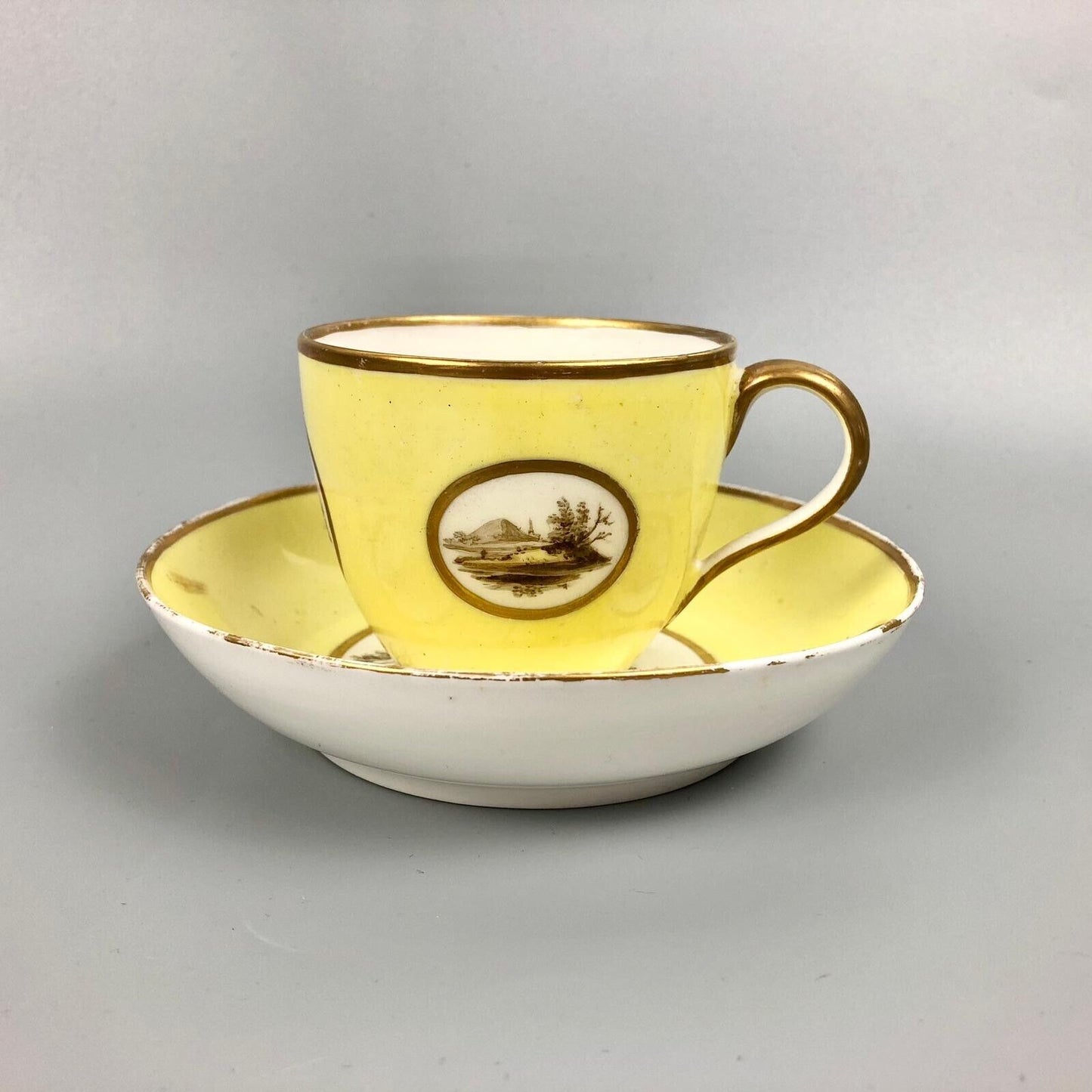 A Pinxton coffee cup and saucer in yellow ground and sepia landscapes. C.1796-9