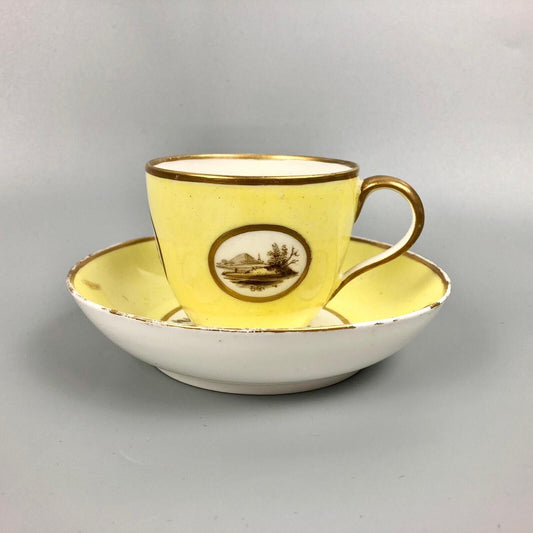 A Pinxton coffee cup and saucer in yellow ground and sepia landscapes. C.1796-9