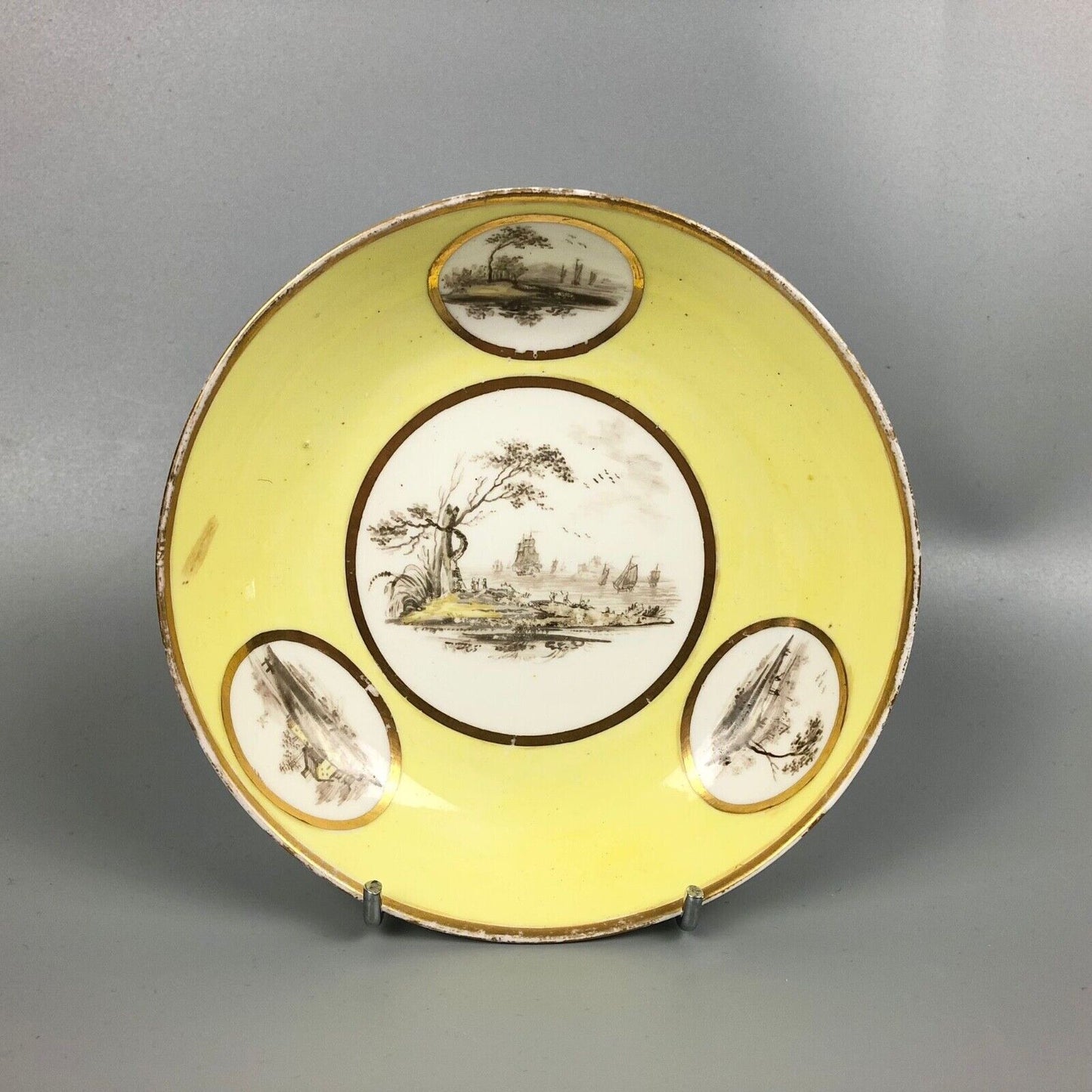 A Pinxton coffee cup and saucer in yellow ground and sepia landscapes. C.1796-9