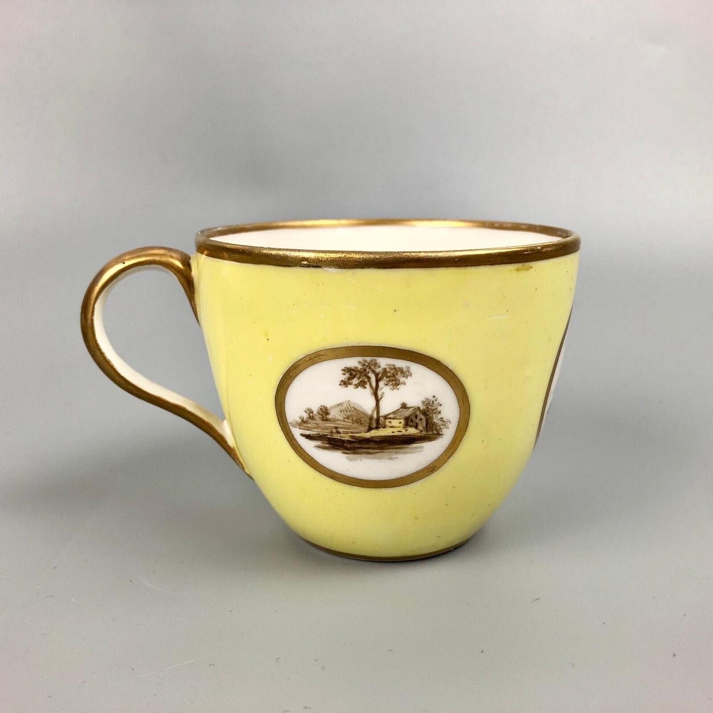 A Pinxton coffee cup and saucer in yellow ground and sepia landscapes. C.1796-9