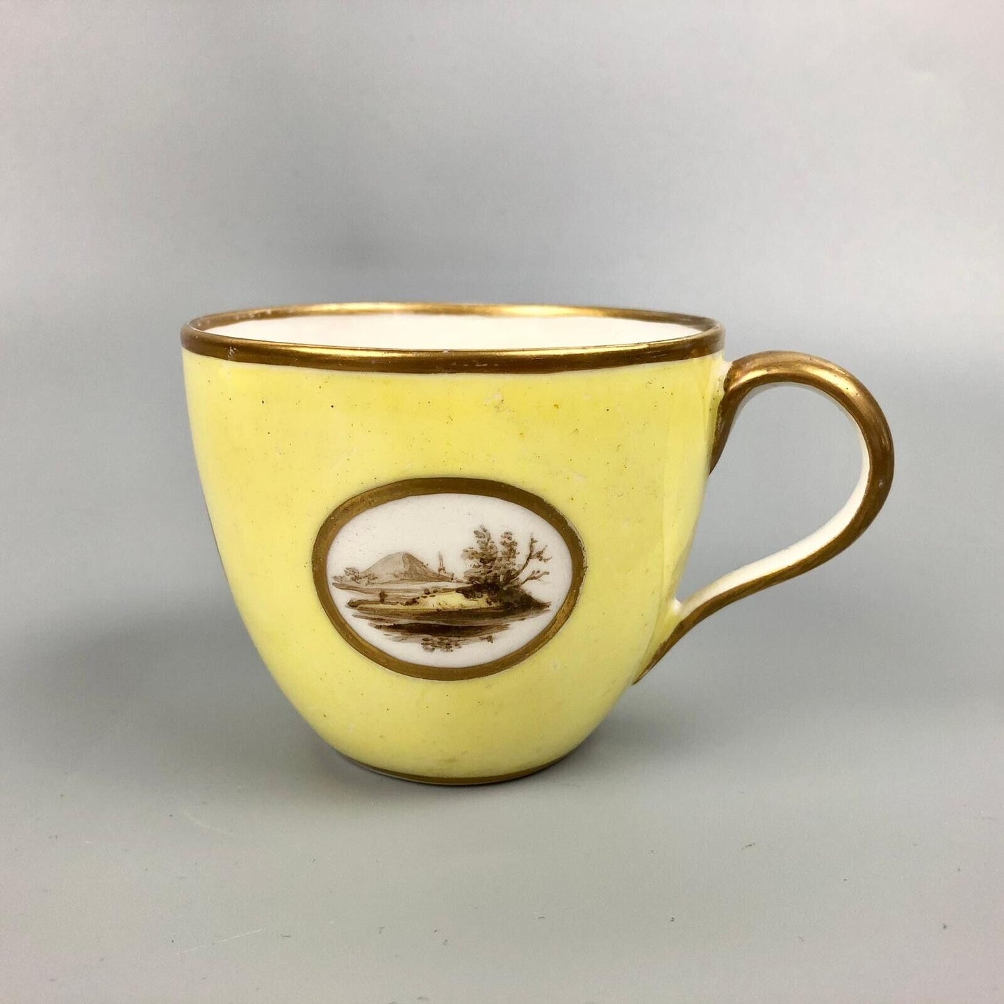 A Pinxton coffee cup and saucer in yellow ground and sepia landscapes. C.1796-9