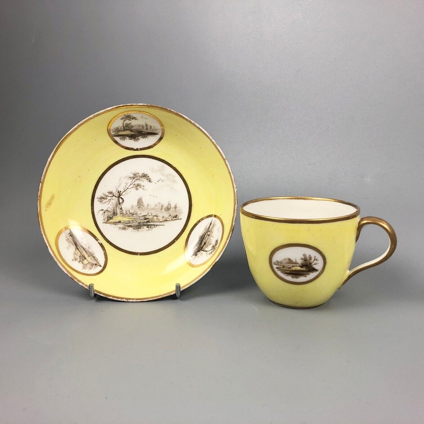 A Pinxton coffee cup and saucer in yellow ground and sepia landscapes. C.1796-9